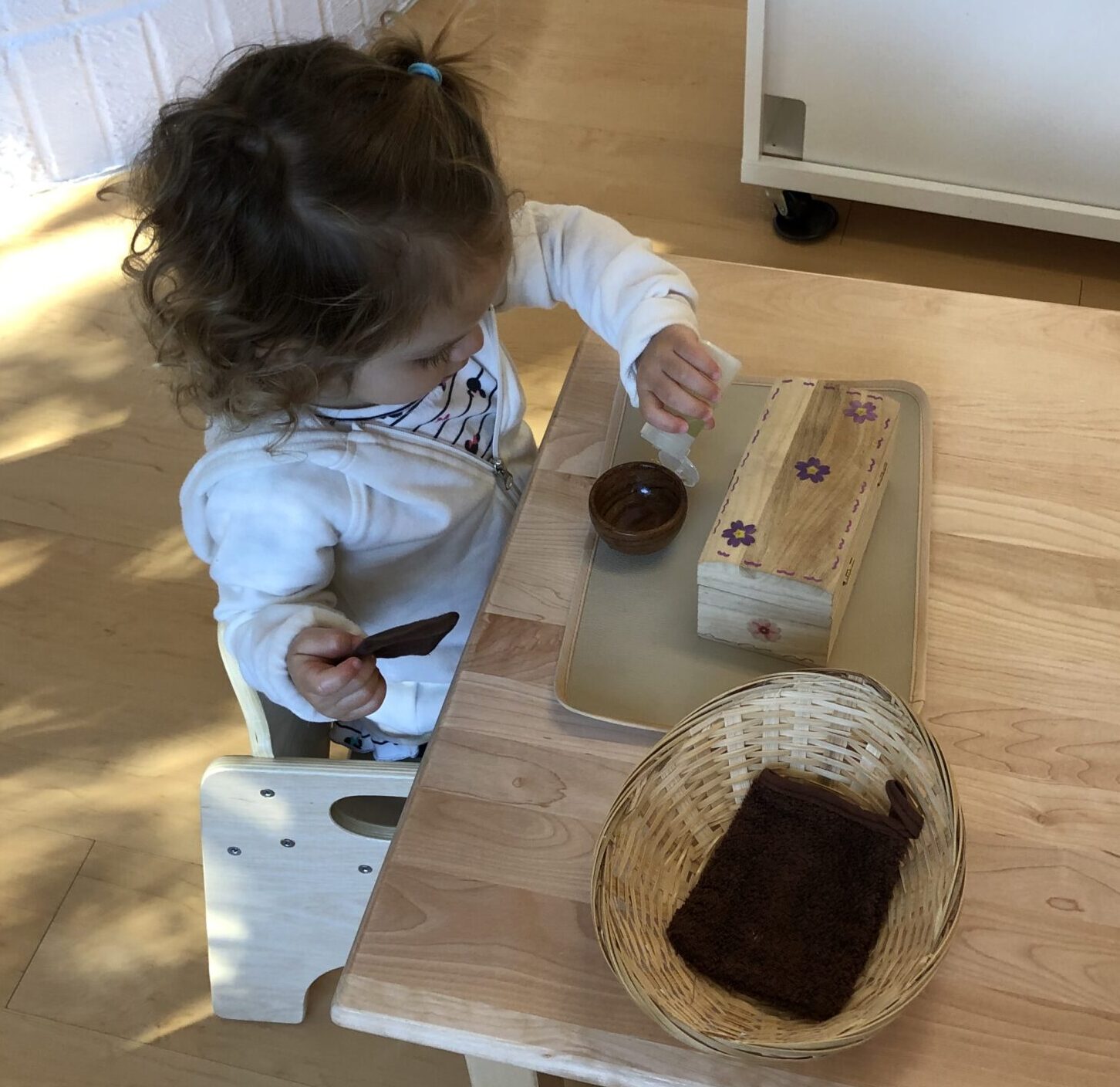 Montessori toddler squirting liquid into a small bowl